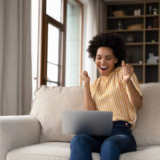 istockphoto-1355293345-612x612 Excited cheerful young Black woman using laptop computer on sofa at home, getting good news, feeling joy, dancing with hands, singing, laughing, making winner gesture, happy to win prize