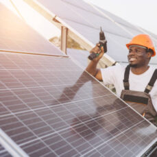 istockphoto-2183295926-612x612 A cheerful technician in a hard hat installs solar panels outdoors. The setting sun adds warmth, highlighting the sustainable energy solution. Perfect for themes of renewable energy.